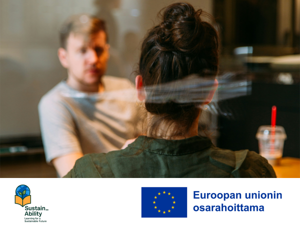 Kaksi ihmistä keskustelee pöydän äärellä ja Sustain_Ability-hankkeen logo ja EU:n osarahoittama -logo.